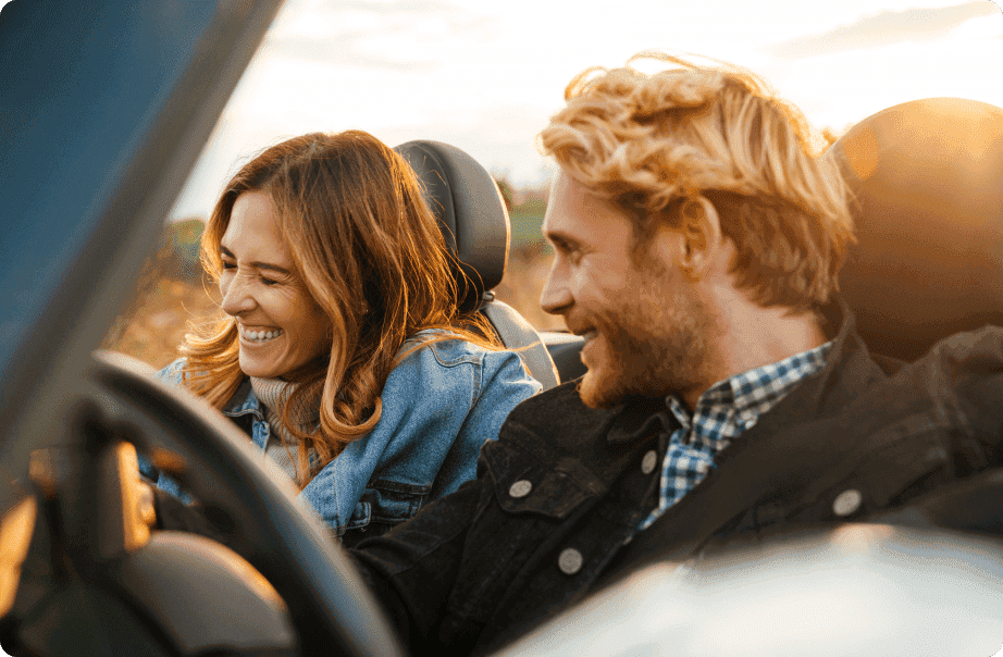 A couple driving a sports car with smiles on their faces