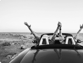 A couple celebrating while driving a convertible with their hands in the air